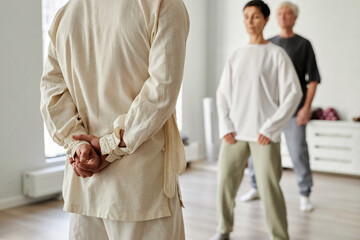 Cropped shot with back view at qigong male master dressed in white apparel with hands behind his...