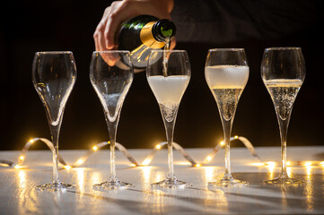 New year party, pouring of brut champagne bubbles cava or prosecco wine in tulip glasses with garland  lights on background