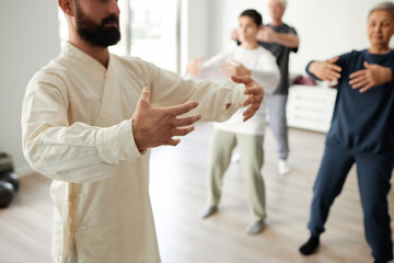 Cropped shot of bearded male qigong master teaching qigong tree pose, students repeating standing...