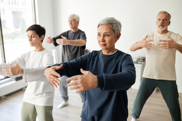 Medium full shot of senior male and female qigong class participants practicing tree pose for...
