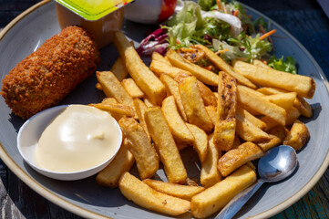 Dutch fast food, deep fried croquettes filled with ground beef meat and french fried potatoes chips served with green salad, close up