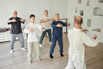 Wide shot of senior people meditating during qigong exercise in fitness studio while male...