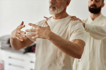 Close up of senior man doing standing meditation exercise during qigong training with master assisting