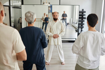 Full shot of male master instructing qigong class participants energy concentration exercise while...