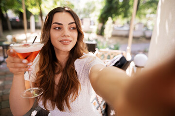 Happy girl taking selfie with cocktail relaxing in cafe at resort, summer vacation concept