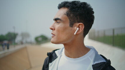 Sporty guy listening music in earphones closeup. Confident fit athlete training