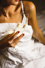Sexy woman posing with a glass of champagne in bed hotel room. Vacation concept