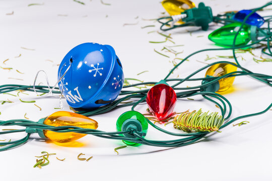Christmas lights, a blue bell ornament and stray pine needles on a white background