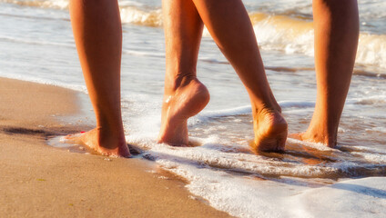 female feet on a sandy beach in the waves of the surf of the sea in summer close up