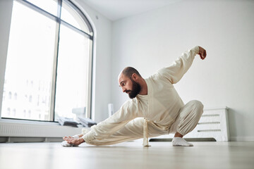 Full shot of bearded male instructor performing qigong snake position on gym floor with arms and...