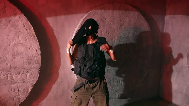 gangster woman in bulletproof vest taking off her balaclava, medium portrait shot in studio