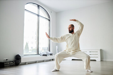 Full length shot of Caucasian adult male qigong master exercising in spacious fitness studio