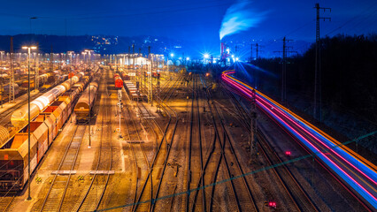 Shunting yard and railway station in Hagen Westphalia Germany at morning blue hour twilight with passing train and factory. Panoramic wide angle night view with long time exposure and colorful lights.