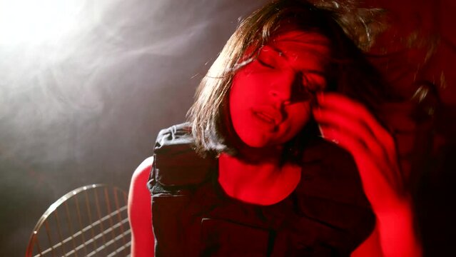 beautiful female terrorist taking off black balaclava from pretty face in dark room with red light