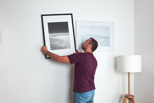 Man hanging pictures on the wall, cleaning and remodeling apartment.