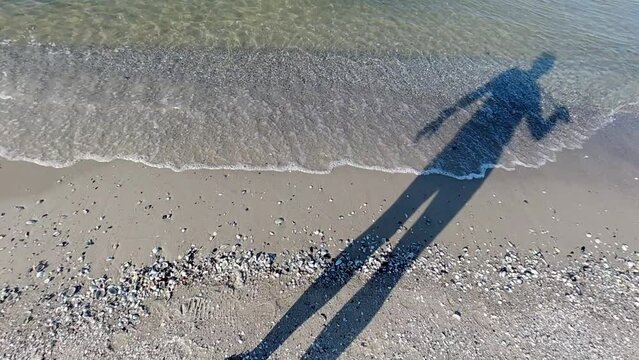 Early morning. Sea surf.  The shadow of a human figure falls on the sand and waves.  Slow motion.