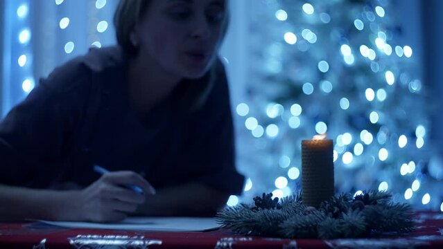 Under a magical Christmas tree, a woman with great tenderness chooses the words for a letter with wishes. Lights and balls create an atmosphere of a real holiday around her. High quality 4k footage