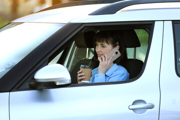 Remote work. Successful businesswoman entrepreneur holds paper cup of coffee while talking on smartphone in comfortable car. Work on road in the midst of traffic jams. Concept of results orientation