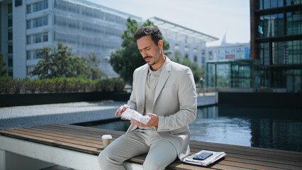 Elegant boss unpacking lunch sunny park. Business man enjoying sandwich at bench