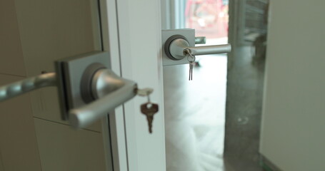 Close-up of a doorknob with a key inserted. Close-up of open transparent glass door and door handle.