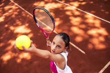 Little child girl playing tennis during practice on clay court