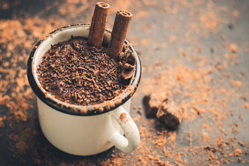 Homemade spicy hot chocolate drink with cinnamon stick, star anise, grated chocolate in enamel mug...