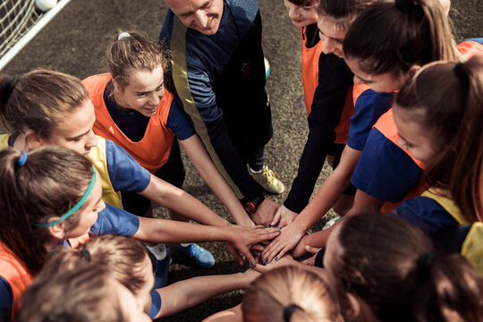 Female soccer team putting hands together with coach
