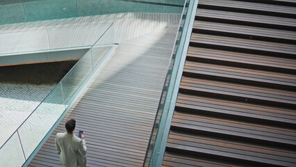 Calm businessman crossing ramp holding smartphone back view. Man walking down