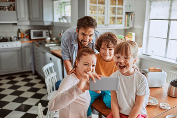 Young family taking selfie during messy breakfast in kitchen