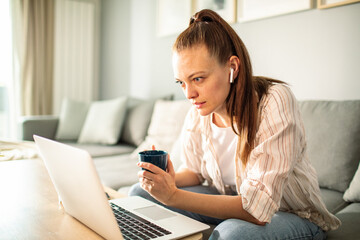 Thoughtful young woman working from home on laptop