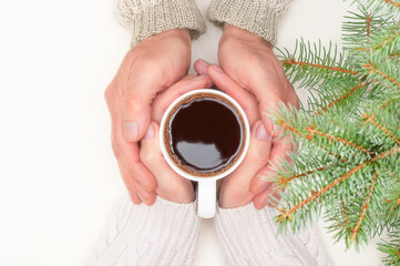 Top view of evergreen branches, man's hands over woman's hands waht hold cup of hot coffee on ivory color background. Cozy home concept at winter and christmas holidays