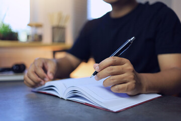 A man uses a pen to write on a notebook to write a memo or compose a song and review goals or plan...