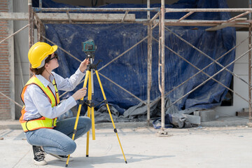 Fototapeta premium Civil engineer woman in vests and helmet safety wear sunglasses using laser level meter at construction site. Forman female working in building workplace.