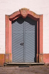 Grey wooden door in a pink baroque sandstone portal with an old keystone on the facade of...