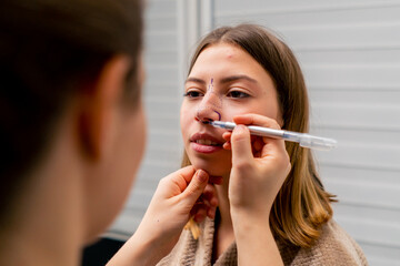 close-up plastic surgeon makes marks on a patient's face during a consultation before a nose...