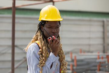 African American female engineer control work by radio communication at construction site, wearing...