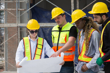 Group of foreman builder at construction site. Male and female engineer holding blueprint and planning work at construction site, wearing safety uniform, helmet