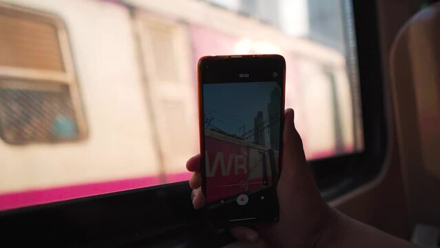POV shot of girl shooting video of Mumbai local train with her mobile phone via train window in Mumbai, Maharashtra, India. Lifestyle in metropolitan city. Girl shooting video of social media.