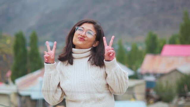 Portrait of happy Indian teenager girl posing with peace sign and pout face. Confident girl outdoors. Influencer girl posing for photo. Indian model, young and stylish in hand gesture for happy memory