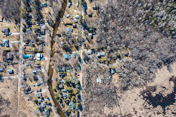 Aerial view of a quaint residential area nestled along a winding river in Tay Township, Simcoe County, Ontario. The landscape shows a blend of rustic charm with homes scattered among bare trees, signa