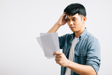 Worried over bills, an Asian man is portrayed in a studio shot, holding a document and appearing...