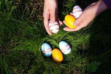 close-up of a woman's hands collecting colorful Easter eggs in the green grass