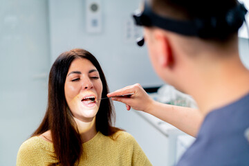 the ENT doctor examines the patient in the office of the clinic, checks the oral and nasal cavity and ear canals with professional instruments - obrazy, fototapety, plakaty