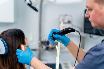 An ENT doctor performs an endoscopy procedure on a patient's ear in a clinic holding a professional...