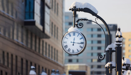 Close up of a snow-covered city clock on a forged pole. Winter postcard of European city street