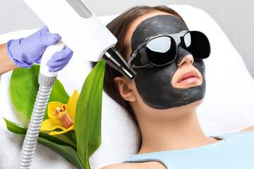 Cosmetologist doing carbon peeling procedure to beautiful blue-eyed girl in a beauty salon....