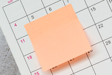 Orange paper sticky note and stuck to a calendar background. Reminder concept.