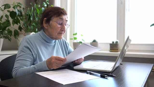 An elderly woman organizes her home office, carefully reviewing papers, bills, and pension insurance documents. She compiles a will. Ideal for content about active and organized lifestyle of seniors.