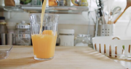 Person pouring fresh organic beverage drink tropical orange juice into transparent glass on wooden board at the kitchen in summer day