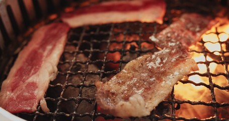 Close up juicy raw meat beef slices BBQ steak on charcoal grill with fire flame smoke, Japanese...
